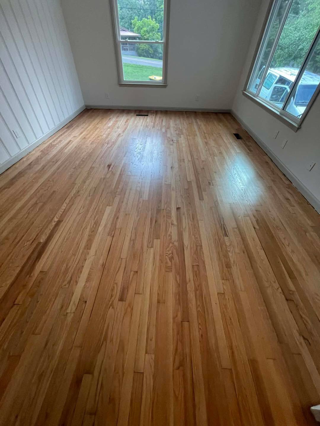 Refinished light hardwood floor in a room with windows and a white paneled wall