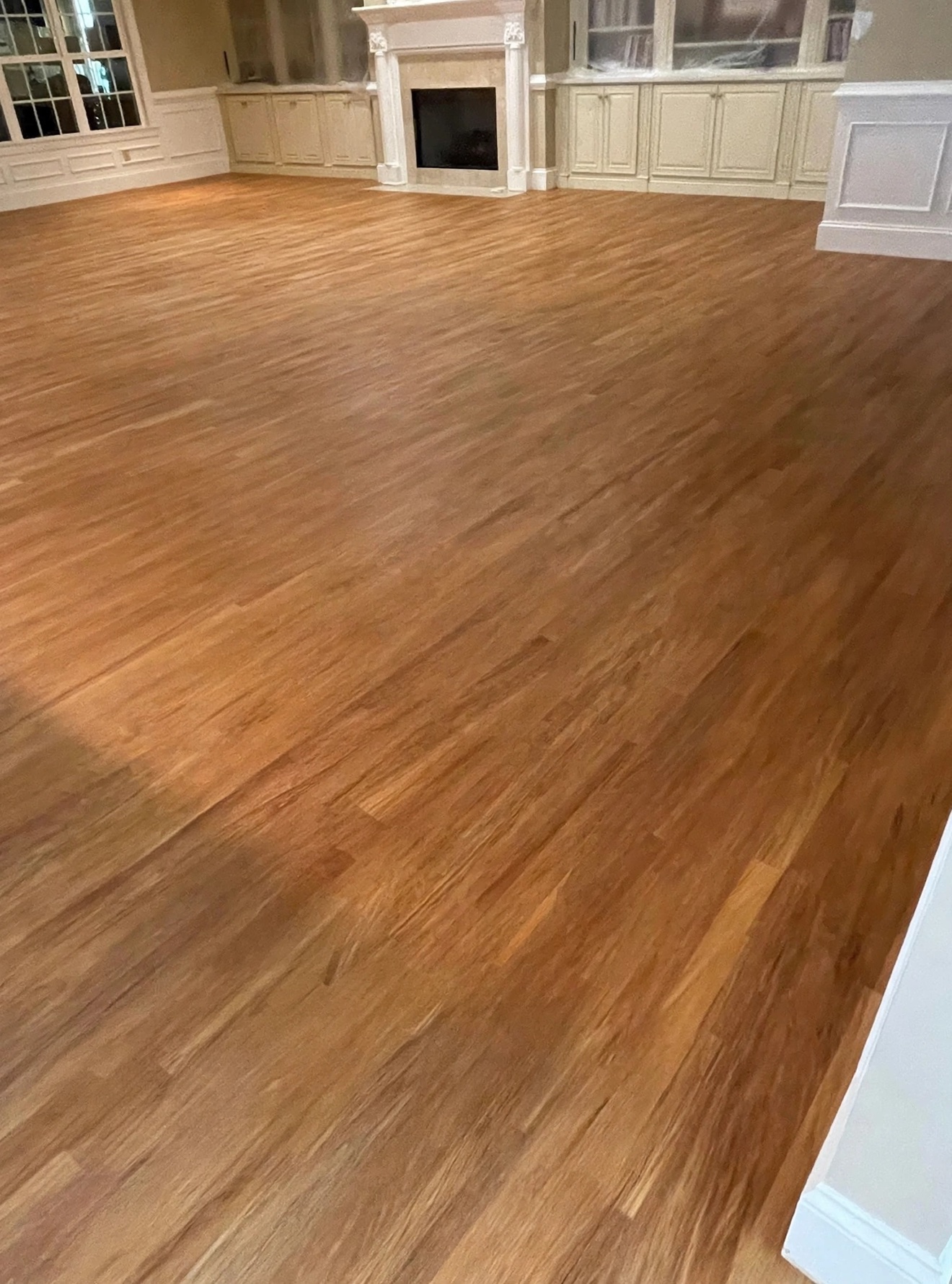 Refinished hardwood flooring in a large living room with a fireplace