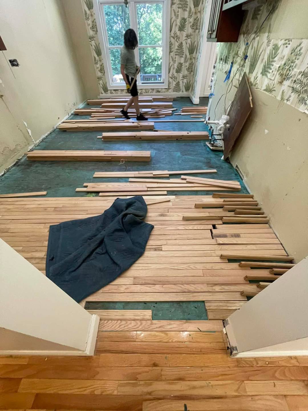 Worker among hardwood boards being installed over green underlayment