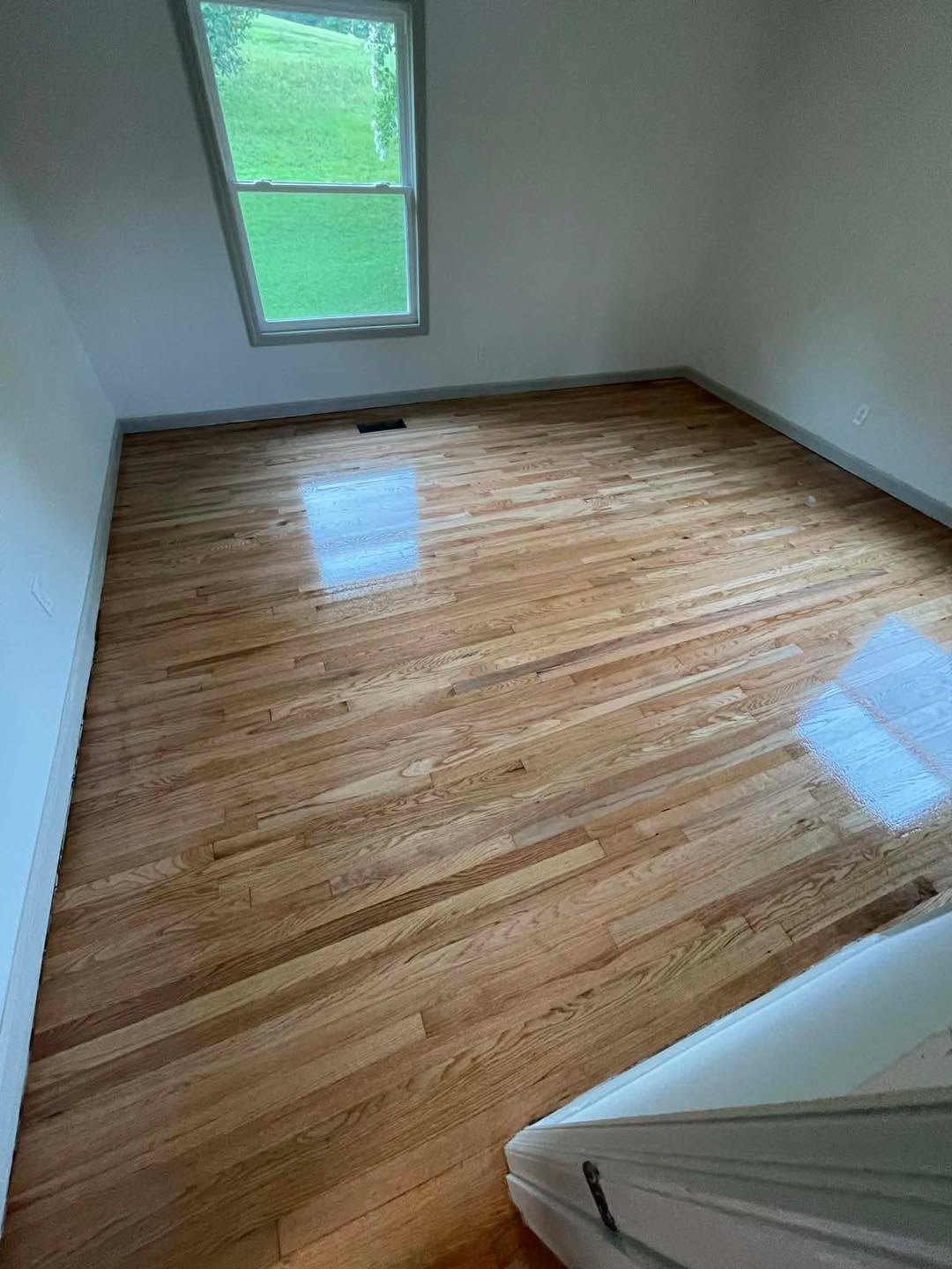 Refinished light hardwood floor in an empty room with a window view