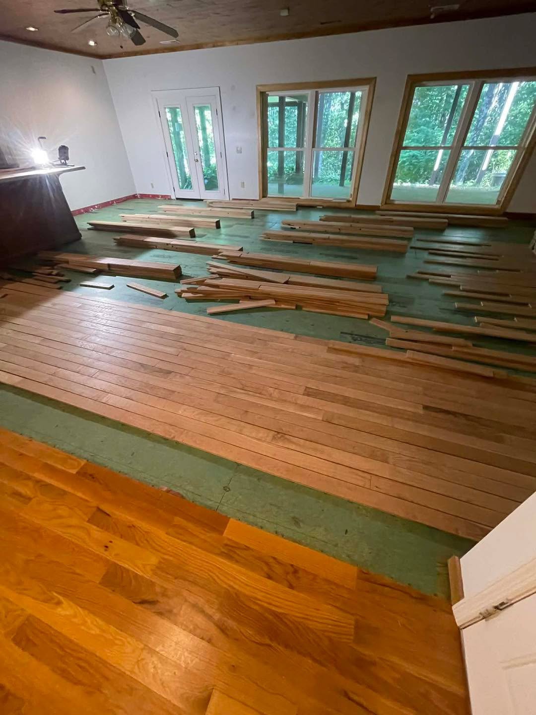 New hardwood boards being installed over green underlayment in a large room