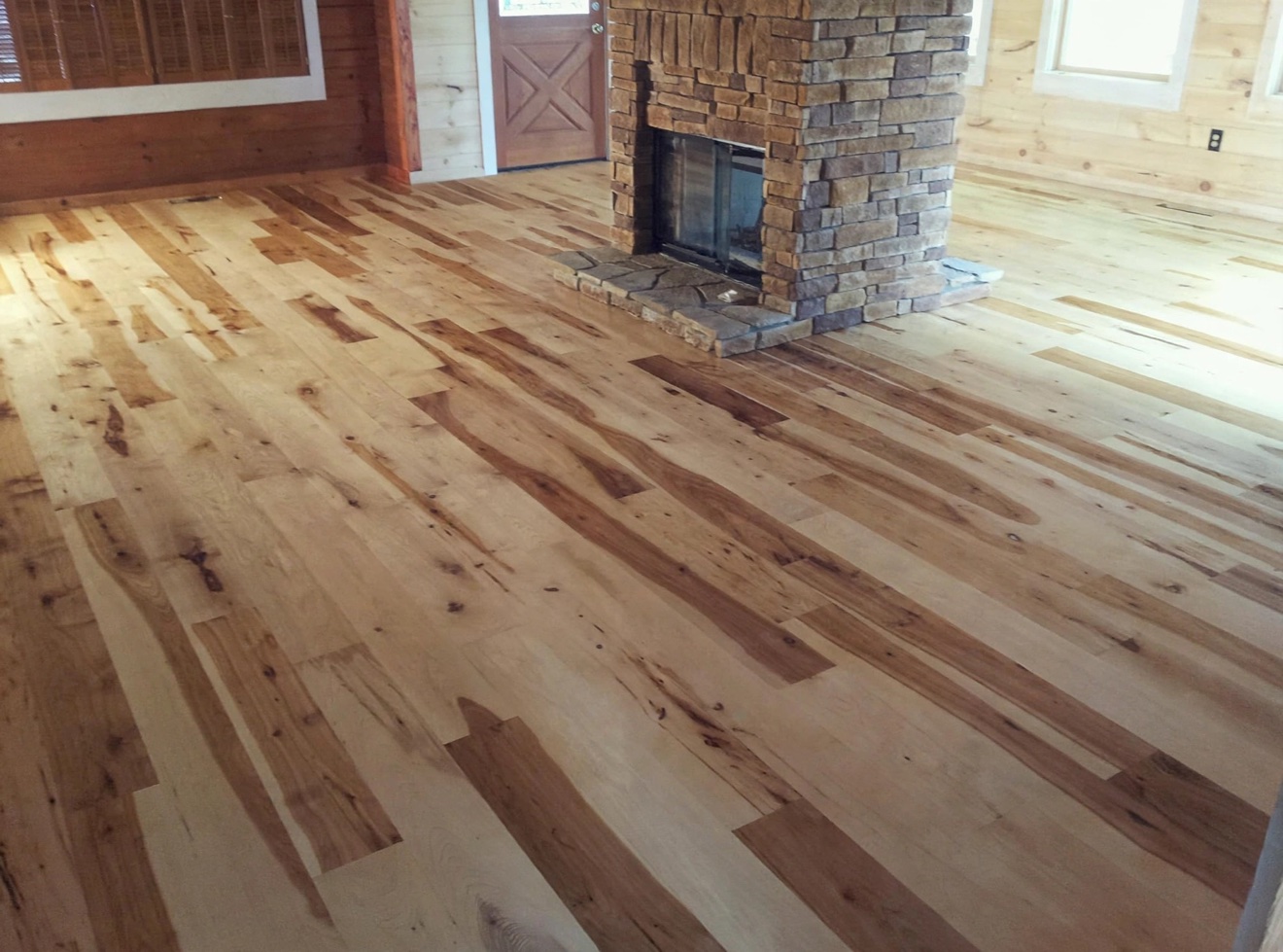 Rustic hardwood flooring in a living room with a stone fireplace