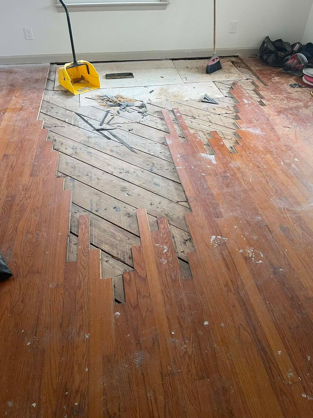 Hardwood floor repair in progress with boards partially removed, a yellow dustpan, a broom, and tools on the floor