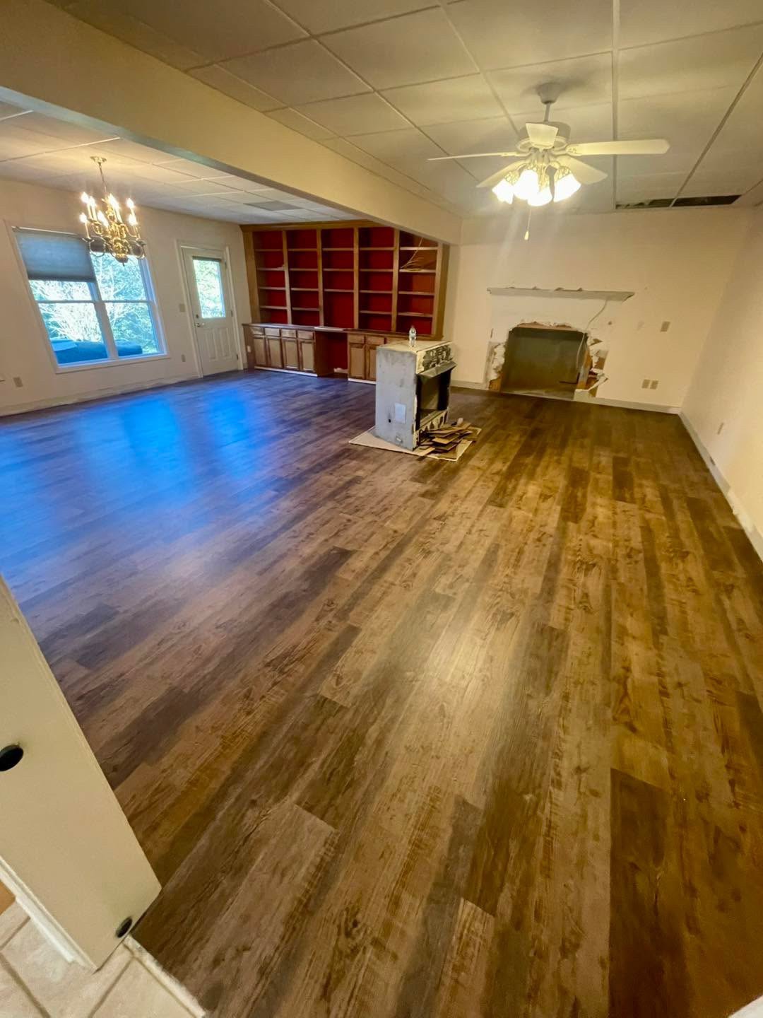 Large room with dark wood-look plank floor, red built-in bookshelves, fireplace work in progress