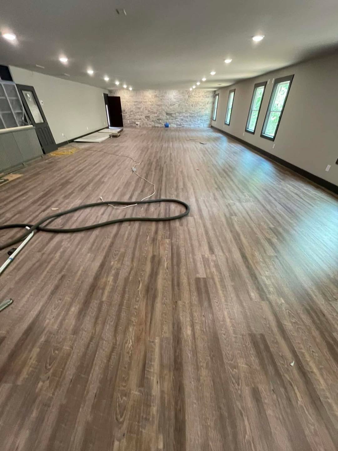 Very large open room with gray-brown wood-look plank floor and stone accent wall